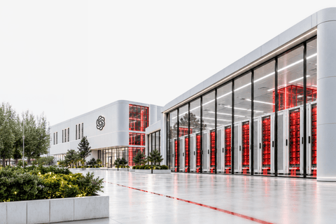 A bright white data centre building with rows of red-lit server racks visible through floor-to-ceiling glass